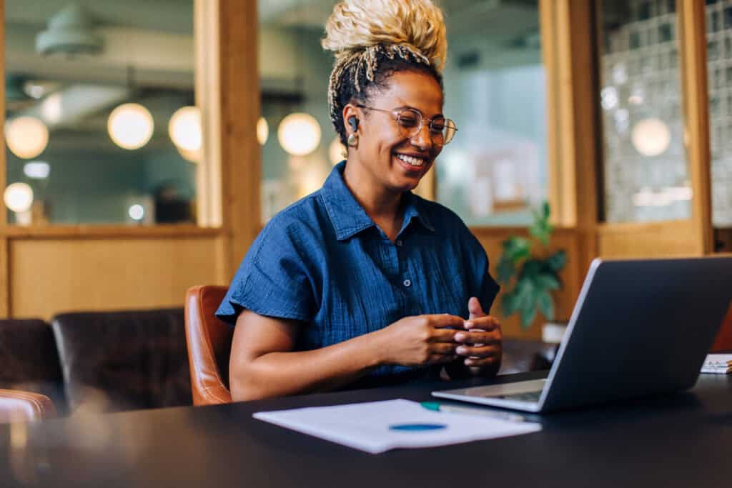 Smiling woman working on laptop in a modern office setting.