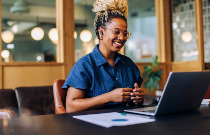 Smiling woman working on laptop in a modern office setting.